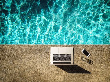 havuz başında dizüstü bilgisayar ve cep telefonu