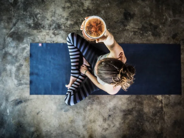 woman drinking coffee sitting on yoga mat