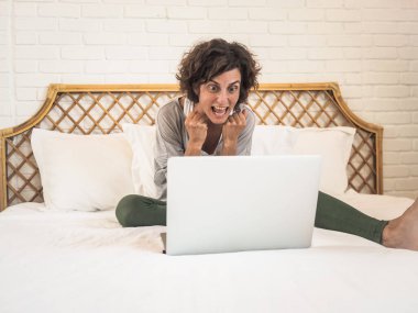 Heyecanlı kadın dizüstü bilgisayarla çalışıyor yatakta oturuyor, ev konsepti üzerinde çalışıyor, karantina altında.