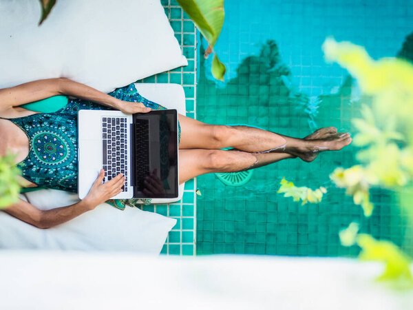 woman working online with laptop sitting at a blue water pool