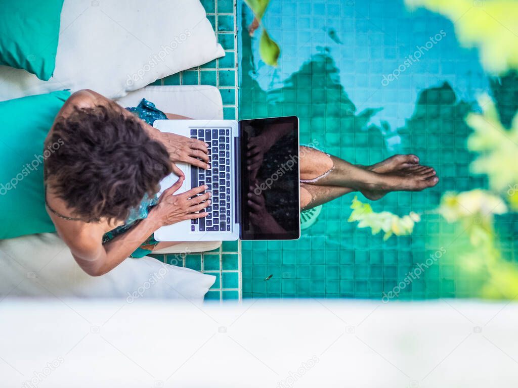 woman working online with laptop sitting at a blue water pool