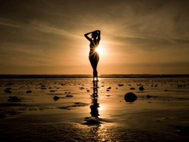 Gün batımında kumsalda yoga yapan genç bir kadın. 