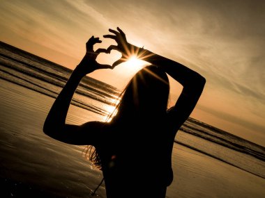 Gün batımında kumsalda yoga yapan genç bir kadın. 