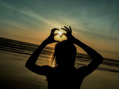 Gün batımında kumsalda yoga yapan genç bir kadın. 