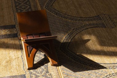 Kuran için ahşap süsleme standı, camide bir halıyla yerde..