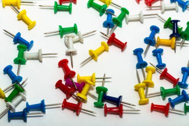 Kağıtları tutturmak için keskin bir iğne. Renkli kırtasiye düğmeleri açık arkaplanda serili. Eğitim için karanfiller. Kağıt iliştiriyorum. Ofis sayfası.