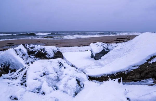 雪が付いている浜の冬景色には 岩と背景に不機嫌な空が覆われています ニュージャージーのサンディ フック ビーチ — ストック写真