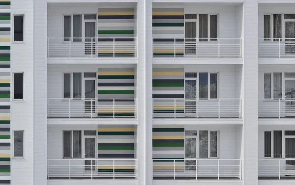 Facade of a public building. Background, texture.Part of a building with white siding. Three floors, Windows and balconies. The walls of the balconies are colored with horizontal stripes.