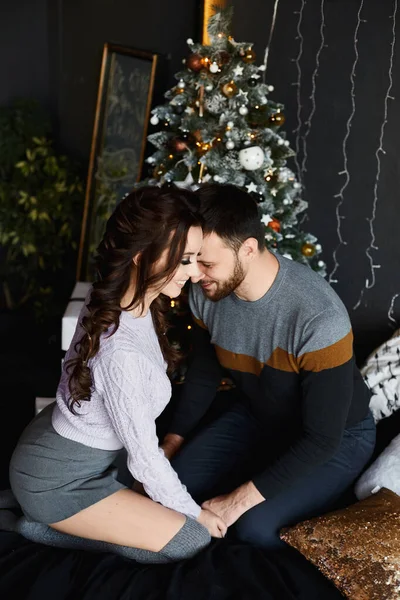 Young beautiful lovers in the Christmas interior. Handsome man and young beauty in stylish outfit spending Christmas evening together in the cozy interior decorated for New year holidays. — Stock Photo, Image