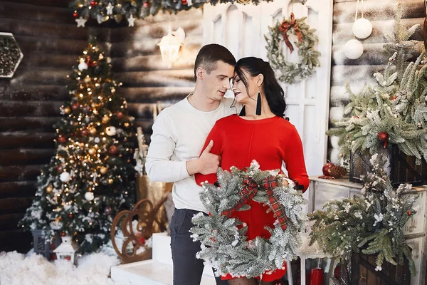 Giovane coppia innamorata che si abbraccia e posa vicino a un albero di Natale ben decorato. Bella giovane donna e bell'uomo che tiene la ghirlanda di Natale e posa all'interno decorata per il nuovo anno . — Foto Stock