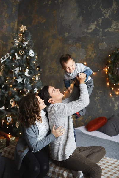 Le père, la mère et leur petit fils s'amusent à l'intérieur de Noël. Le concept de vacances en famille. Jeunes parents et le bébé garçon câlins ensemble à l'intérieur décoré pour le Nouvel An . — Photo