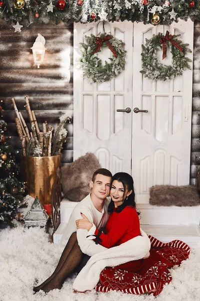 Милая пара обнимает друг друга на фоне рождественских украшений. Красивый мужчина и брюнетка молодая женщина в красном платье и чулках, празднующих зимние праздники и Новый год — стоковое фото