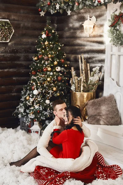 Doux couple s'embrassant sur fond de décorations de Noël. Beau homme et jeune femme brune en robe rouge et bas célébrant les vacances d'hiver et le Nouvel An — Photo