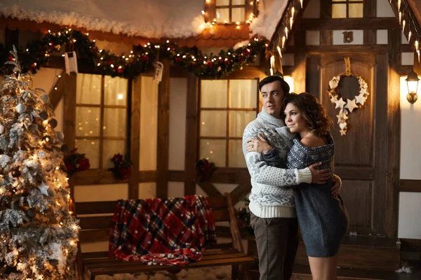 Joyeux jeune femme en robe tricotée scandinave et beau petit ami en pull posant dans la maison de Noël décorée. Couple romantique célébrant le Nouvel An et les vacances d'hiver dans l'intérieur décoré . — Photo