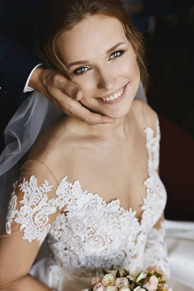 Tender wedding portrait. Beautiful young bride leaning on grooms hand and keeping wedding bouquet. Bridal bouquet of pink and white rose flowers in the hands of model girl in trendy wedding dress.