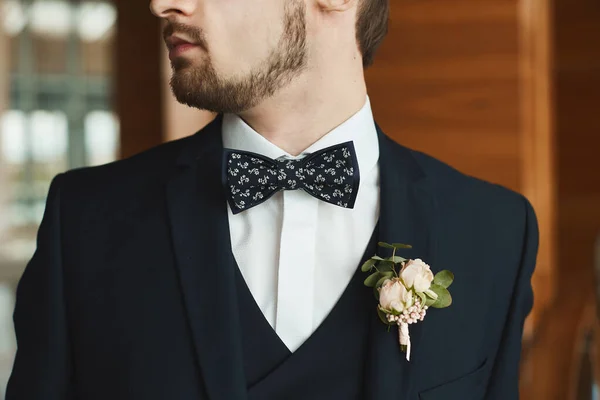 Красивий стильний бородатий чоловік в смокінгу і краватці з бутоньєрою. Молодий бізнесмен в спеціальному смокінгу. Красивий наречений зі стильною бородою у весільному костюмі перед церемонією одруження. Чоловіча мода . — стокове фото