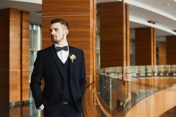 Όμορφος κομψός γενειοφόρος άντρας με σμόκιν και παπιγιόν με μπουτονιέρα. Νεαρός επιχειρηματίας με σμόκιν. Όμορφος γαμπρός με κομψή γενειάδα σε γαμήλιο κοστούμι πριν από την τελετή του γάμου. Ανδρική μόδα. — Φωτογραφία Αρχείου