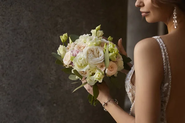 Linda jovem segurando lindo buquê de flores macias de rosas frescas, peônias, flores de eucalipto em tons de rosa pastel e creme em um fundo de parede cinza. Buquê de casamento. Flores nupciais — Fotografia de Stock