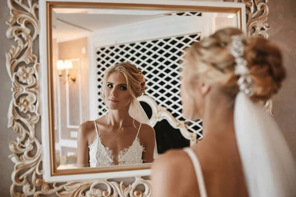 Luxuriöses blondes Model-Mädchen mit platinblonden lockigen Haaren, das im Vintage-Interieur in den Spiegel blickt. Junge blonde Frau blickt ihr Gesicht durch den Spiegel an. Morgenvorbereitung der jungen Braut — Stockfoto
