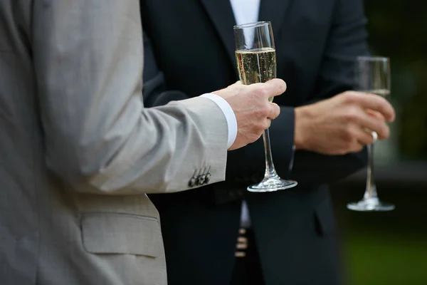Young man in suit holding glass of champagne. Close up of male hand holding glass of champagne. Man is standing in elegant suit