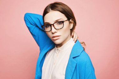 Zarif gözlüklü, zarif makyajlı ve pembeli, modaya uygun mavi ceketli genç bir kadın. Pembe bluzlu, mavi ceketli, pembe arka planda motif gözlüklü, izole bir kız. Uzayı kopyala Bahar