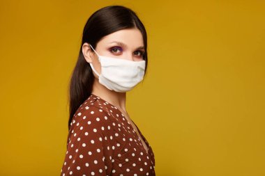 Closeup portrait of a young woman in a protective face mask isolated at the yellow background with copy space. Model girl in a medical mask. Concept of protection against flue, virus and epidemic.