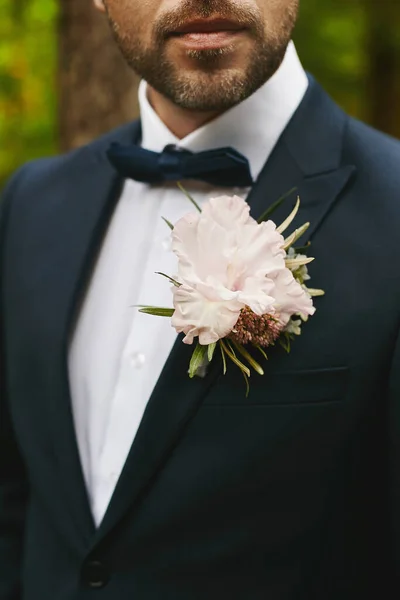 Κομψός γενειοφόρος γαμπρός με μαύρο κοστούμι με παπιγιόν και λευκό μπουτονιέρα στο σακάκι του - λεπτομέρειες γάμου — Φωτογραφία Αρχείου
