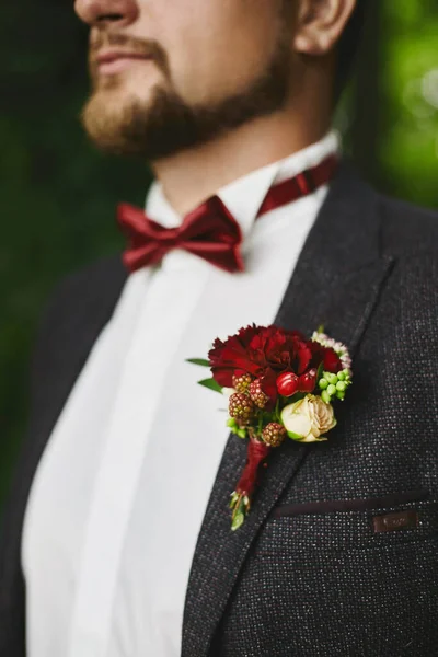 Стильний бородатий наречений з червоною пов'язкою і червоною бутоньєрою на куртці - весільні деталі — стокове фото