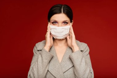 Portrait of a young woman in a protective face mask isolated at the red background with copy space. Model girl in a coat and medical mask. Concept of protection against flue, virus and epidemic