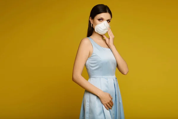 Mujer joven que lleva una máscara facial con respirador para prevenir la enfermedad de la gripe debido a un brote de Coronavirus. Retrato de modelo niña en un vestido y respirador aislado sobre fondo amarillo. Epidemia de gripe — Foto de Stock