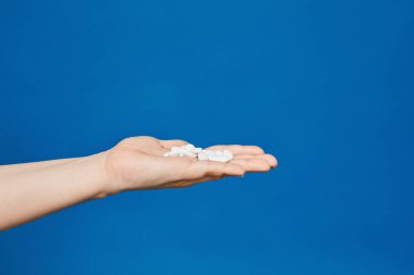 Çekimin sol tarafına uzanan açık dişi avucundaki beyaz haplar mavi arka planda izole edilmiş. Virüs ve grip için ilaçlar. Mevsimsel hastalık. Kopya alanı ile tıbbi reklam