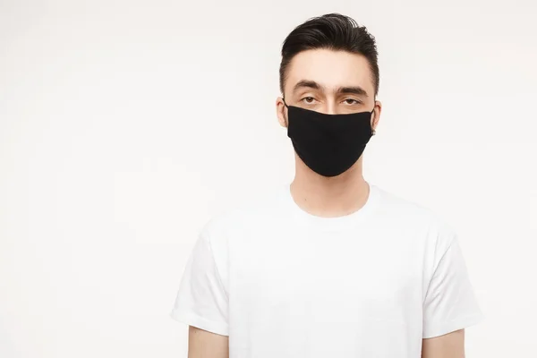 Молодий чоловік у білій футболці та чорній захисній масці ізольовані на білому тлі. Концепція здорового способу життя, сезонні хвороби та концепція сезонного грипу. Чоловік носить медичну маску для запобігання зараженню — стокове фото
