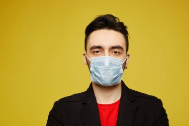 Portrait of handsome young man in black protective mask looking in camera, isolated on yellow background. Seasonal illness and seasonal flu prevention. clipart