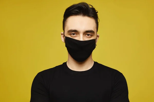 Красивий чоловік у чорній футболці та чорній захисній масці ізольовані на жовтому тлі. Сезонні хвороби та концепція сезонного грипу. Концепція способу життя охорони — стокове фото