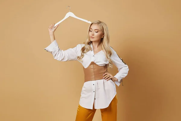 Beautiful young woman in fashionable outfit holding an empty wooden hanger in her hand and expressing that nothing to wear. Shopping concept. Beauty concept. Isolated with copy space.