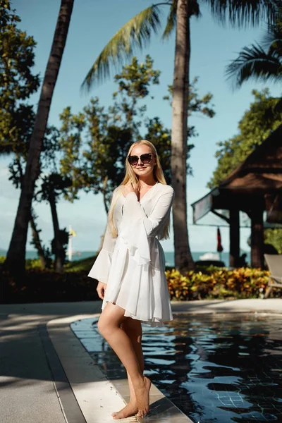 Junge Frau mit blonden Haaren in Peignoir und Bikini posiert am Außenpool im Hotelresort mit Palme. Konzept für Tourismus und Sommerzeit — Stockfoto