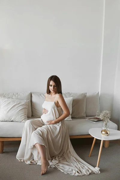 Schwangere Modelmädchen hält liebevoll ihren Bauch und posiert in einem minimalistischen Interieur. Schwangerschaftliches Modekonzept — Stockfoto