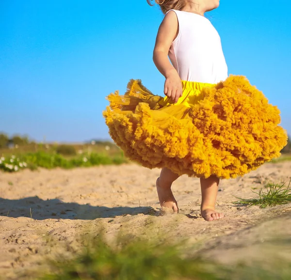 Niña pequeña falda amarillo exuberante arena primavera — Foto de Stock