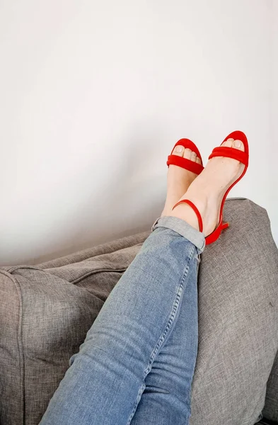 Mulheres pernas sofá roupas jeans sapatos vermelhos stilettos — Fotografia de Stock