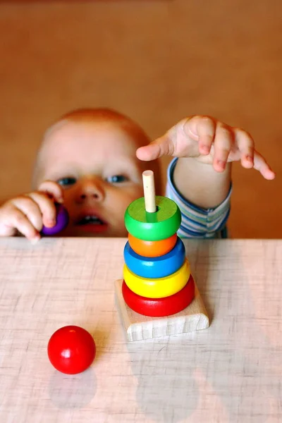 Criança estende a mão atrás de brinquedo de madeira multicolorido em desenvolvimento — Fotografia de Stock