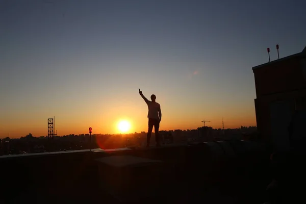 Silhueta homem levantado mão até telhado edifício por do sol — Fotografia de Stock