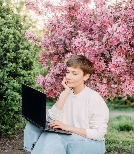 woman with laptop freelance working outside park sakura bloom pink