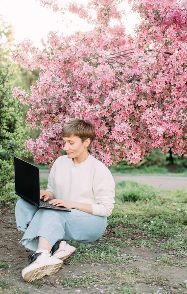woman with laptop freelance working outside park sakura bloom pink