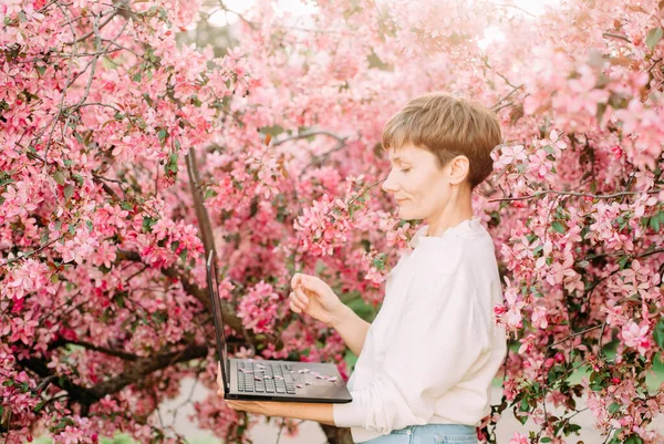 woman with laptop freelance working outside park sakura bloom pink