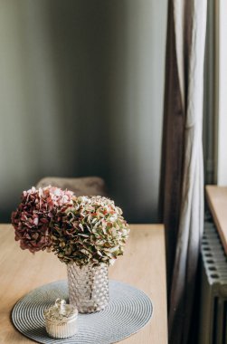Süslü çiçekler cam bir vazoda bir evin içindeki masanın üstünde.