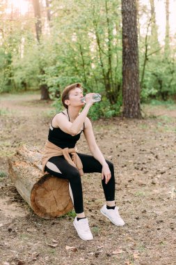 Sporcu ormanda koştuktan sonra dışarıda su içer.