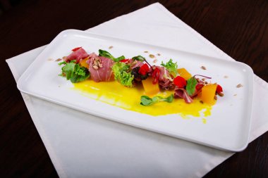 İspanyol jamonu, biber ve tohumlarla süslenmiş beyaz bir tabakta bulunan balkabağı ve sos salatası.