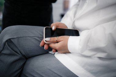 Elinde telefon tutan, kuaför koltuğunda oturan ve düğün saç stilini bekleyen bir kız.