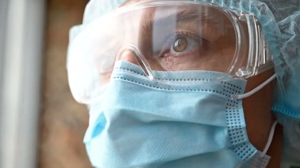 Una mujer con una máscara médica, gafas y una gorra mira a la distancia — Vídeo de stock