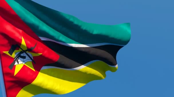 La bandera nacional de Mozambique ondea en el viento contra un cielo azul — Vídeos de Stock